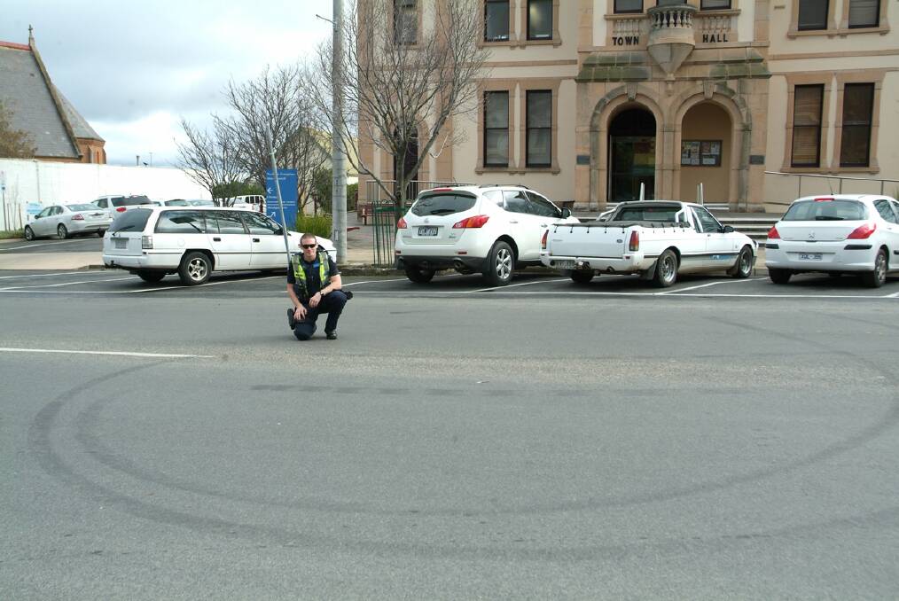First Constable Nathaniel Warren inspects the tyre marks that were left by hoons on the road in Main Street, outside the Stawell Town Hall. Picture: BEN KIMBER.