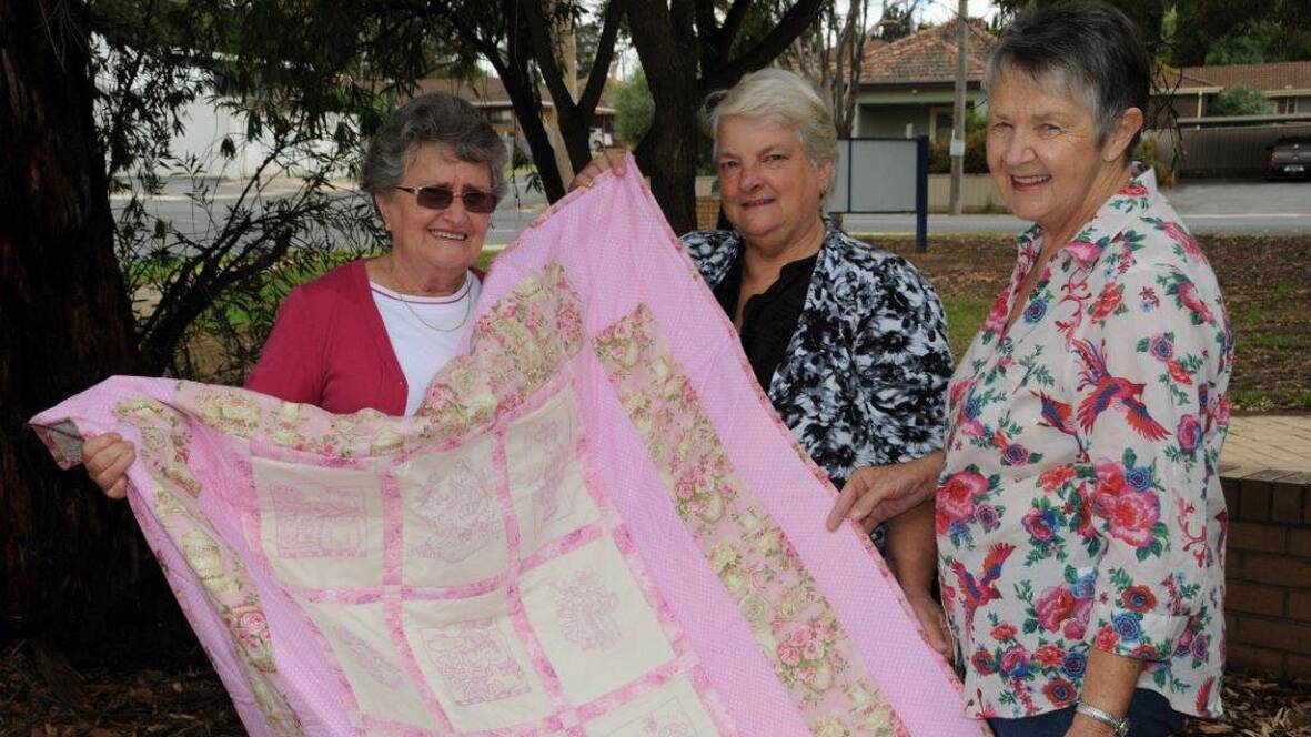 Mother’s Day Classic Walk committee members Pam Byron (left) and Merrilyn Middleton (right) receive the donated quilt from Lyn Keller.