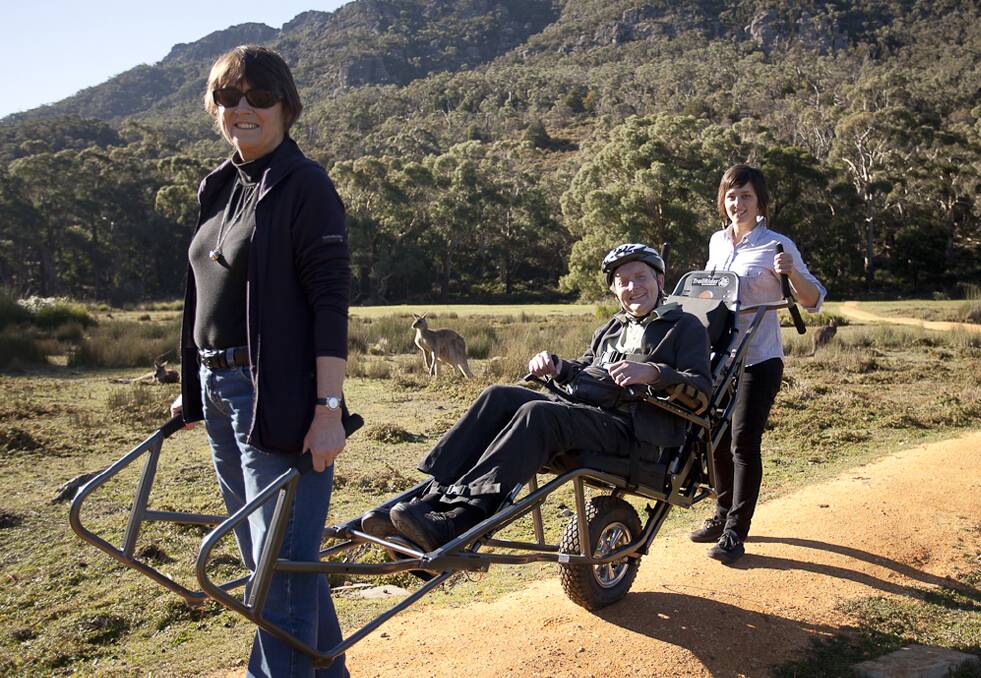 David Stratton takes a ride in the all-terrain wheelchair, with his wife Ros Hart (at the front) and Parks Victoria staff member Megan Calabro.